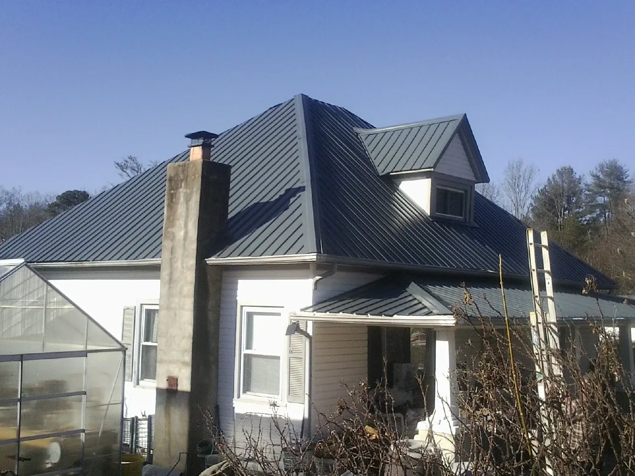 Dark blue standing seam metal roof on a white farmhouse with dormer — Slate & Tile Roof Repair by Roofing Brothers in Fairmont