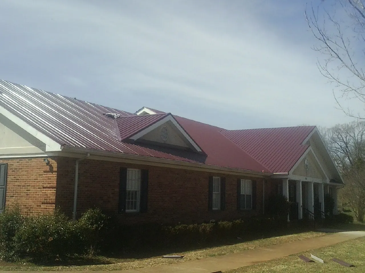 Red metal roof with gabled entries on a long brick building, from a Hail Damage Roof Repair job in Fairmont