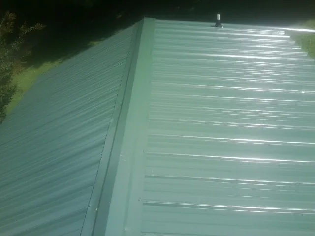 New green metal panels meeting at the ridge of a roof — Flat Roof Repair work by our crew in Fairmont