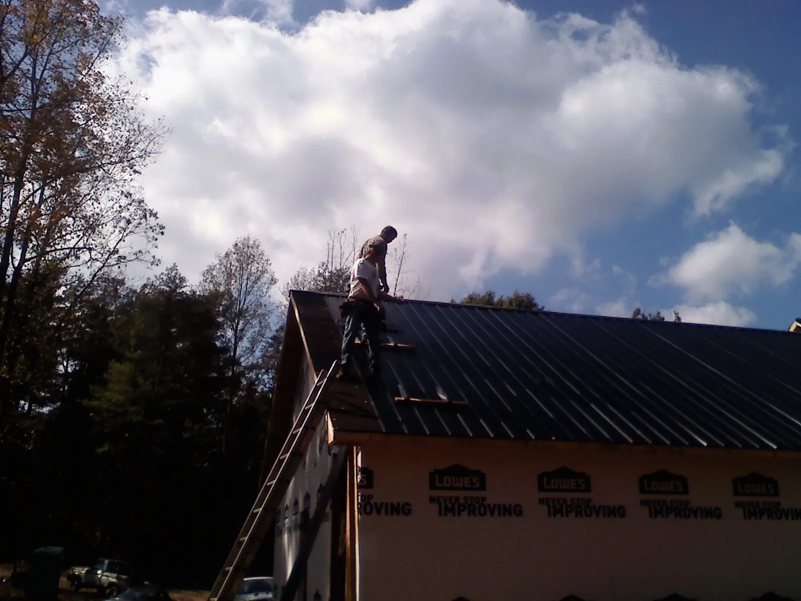 Roofer fastening dark metal panels high against a cloudy sky, from a Roof Inspection job in Fairmont