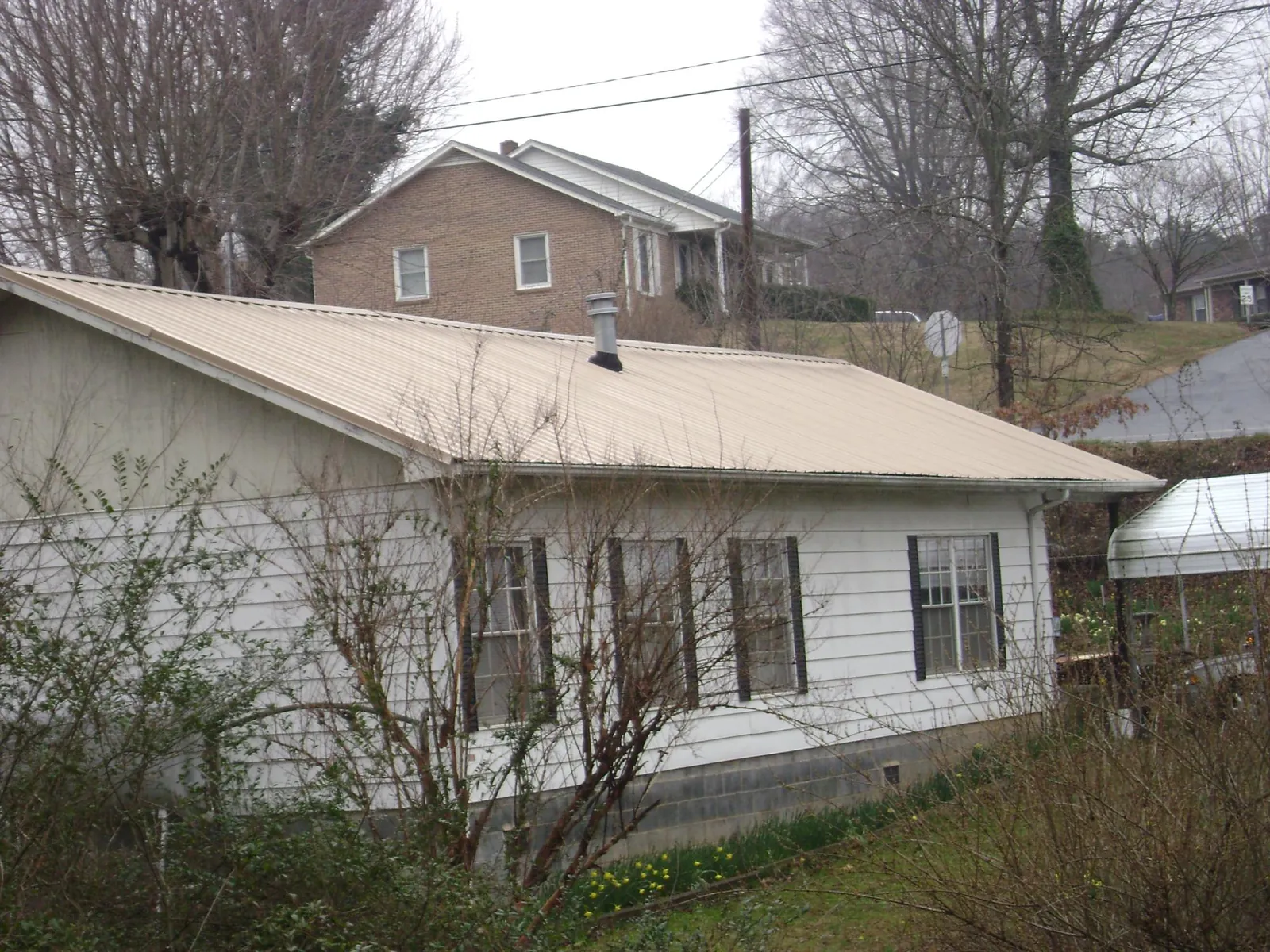 Tan metal roof on a white sided house set into a hillside — Commercial Roofing by Roofing Brothers in Fairmont