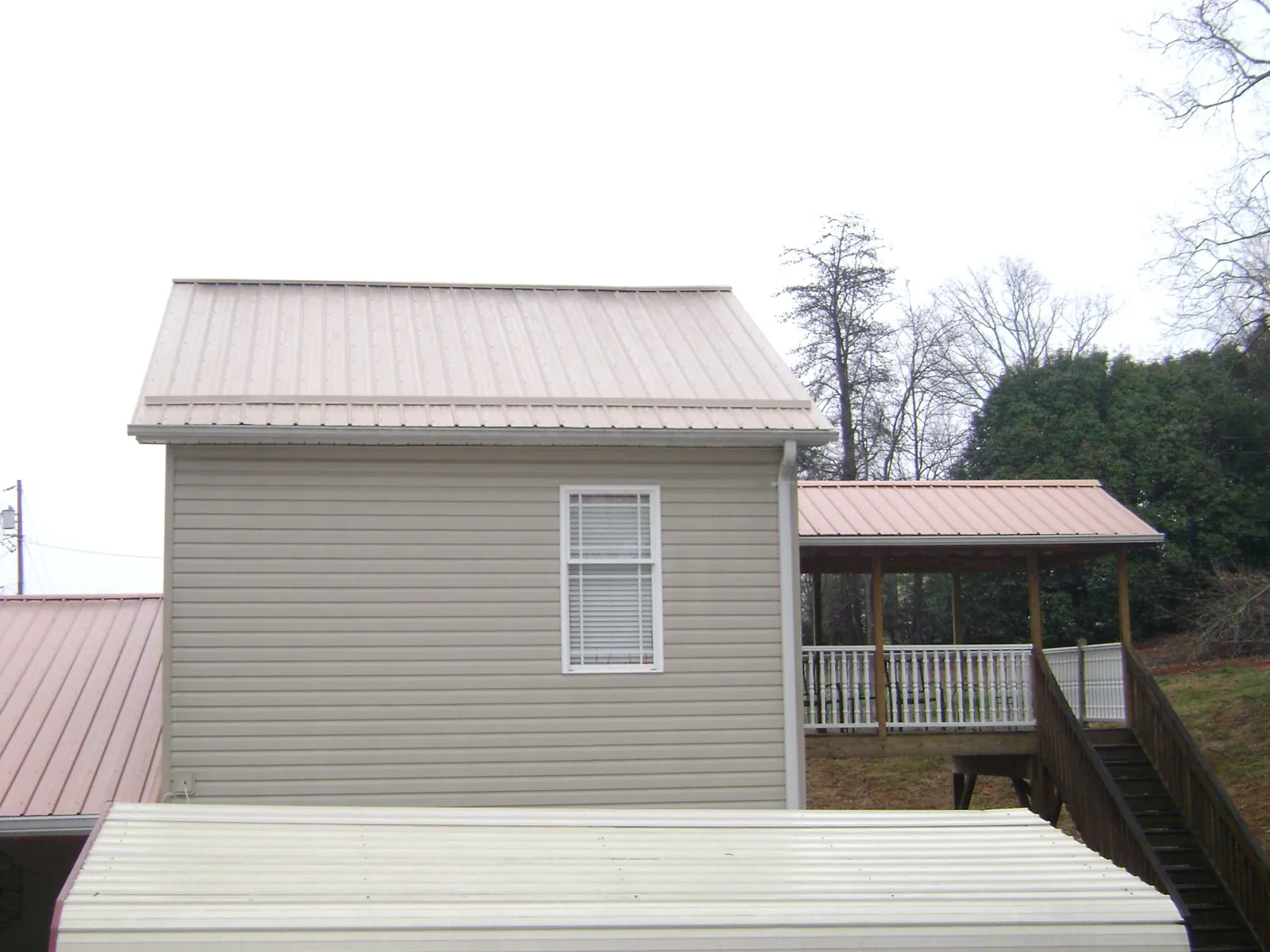 Tan metal roofs on a two story addition and attached porch, from a Roof Replacement job in Fairmont